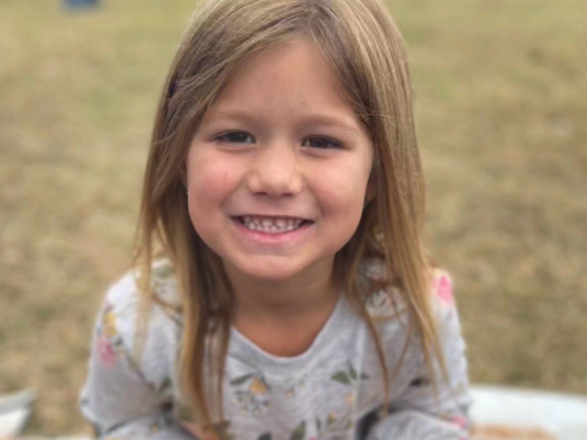 Smiling child in a light shirt sitting outdoors on grass with a blurred background