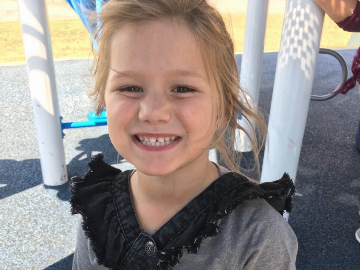 Smiling child in a gray dress standing on a playground with white poles