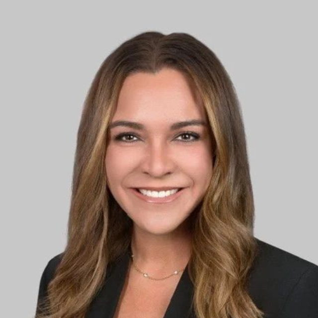 Smiling woman in a black blazer against a gray background.
