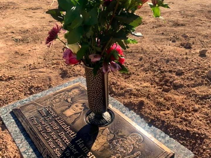Memorial plaque on dry ground with a floral arrangement in a vase on top
