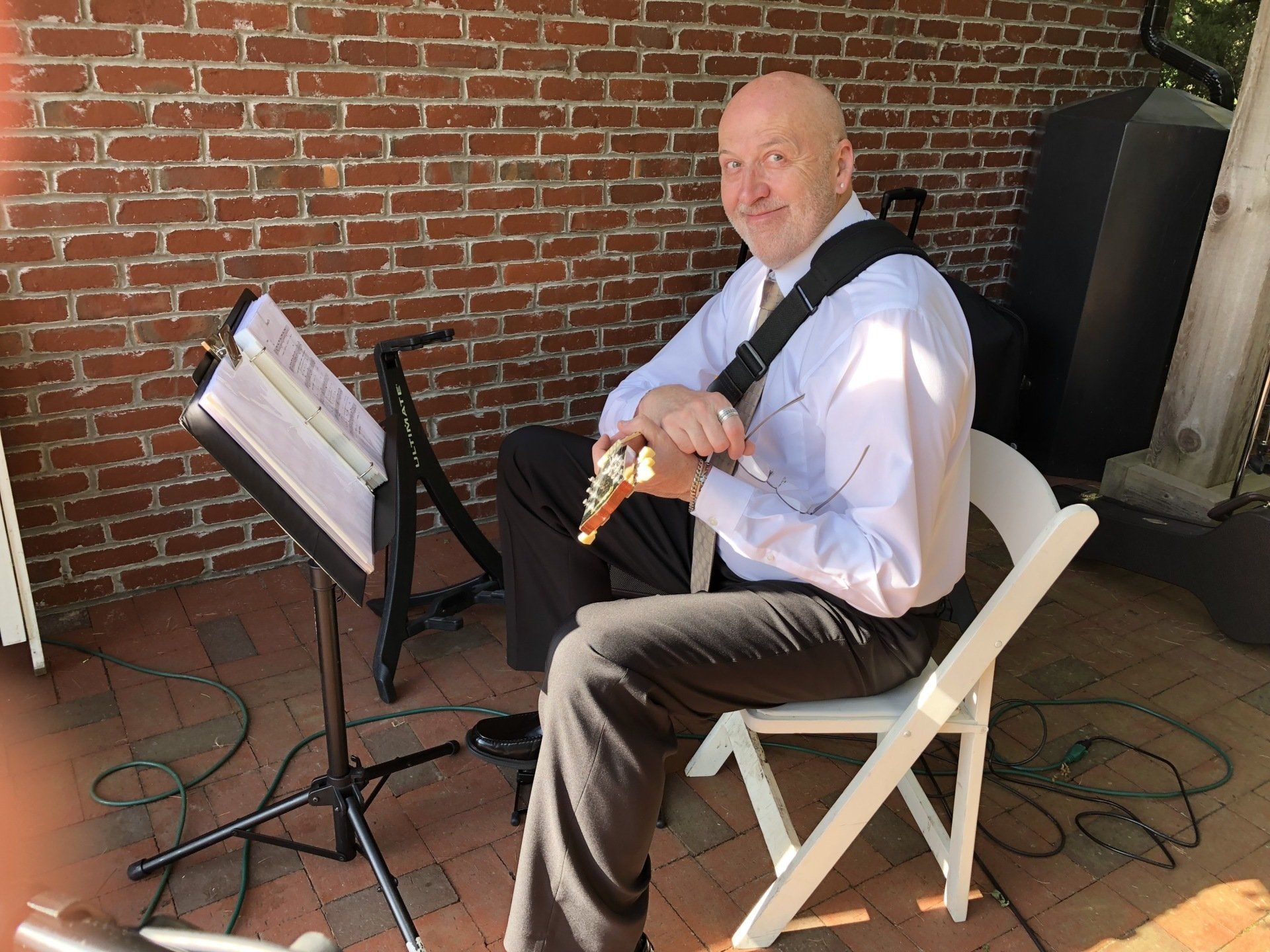 A man is sitting in a chair playing a flute in front of a brick wall.