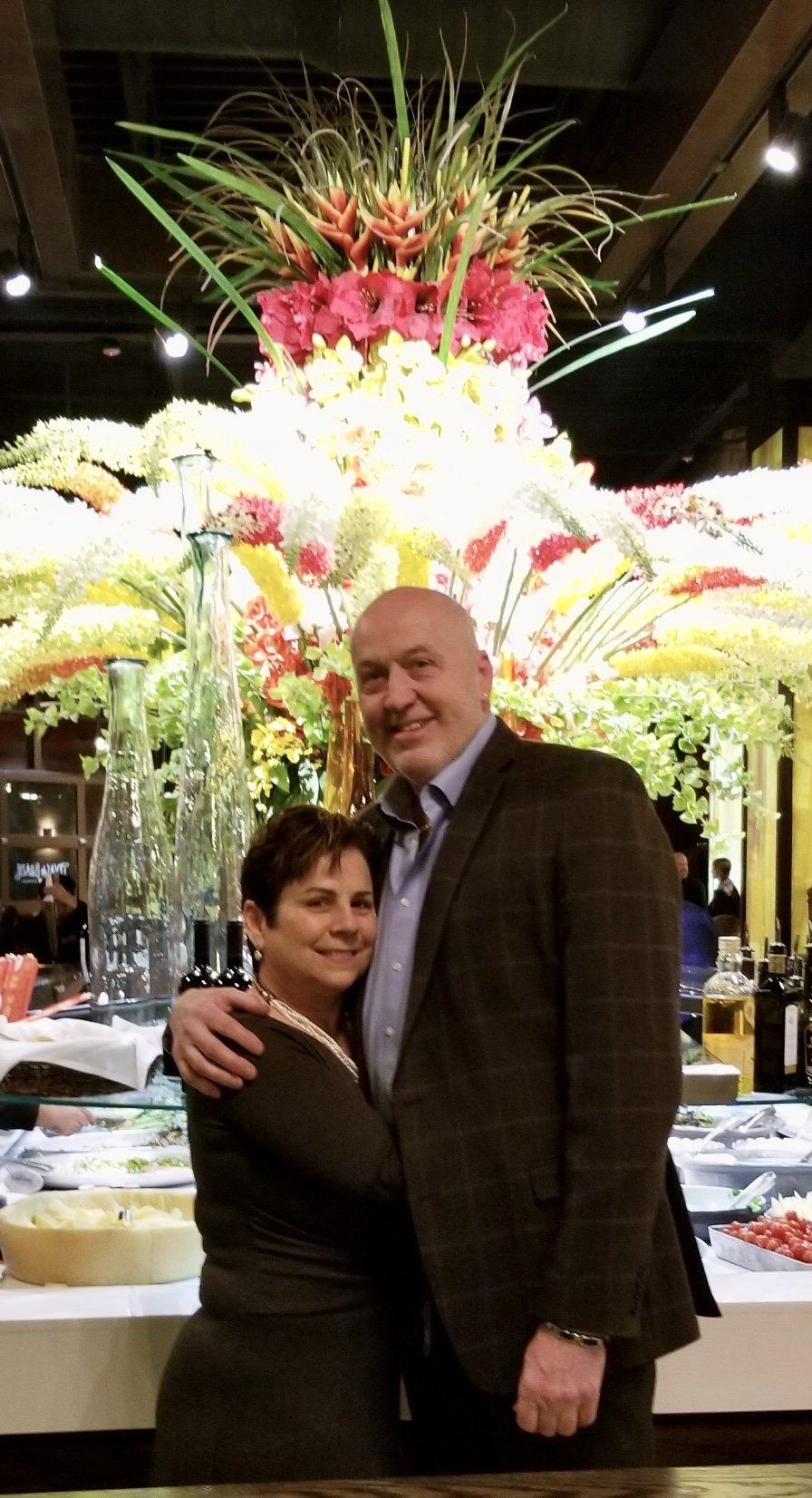 A man and woman are posing for a picture in front of a large vase of flowers.