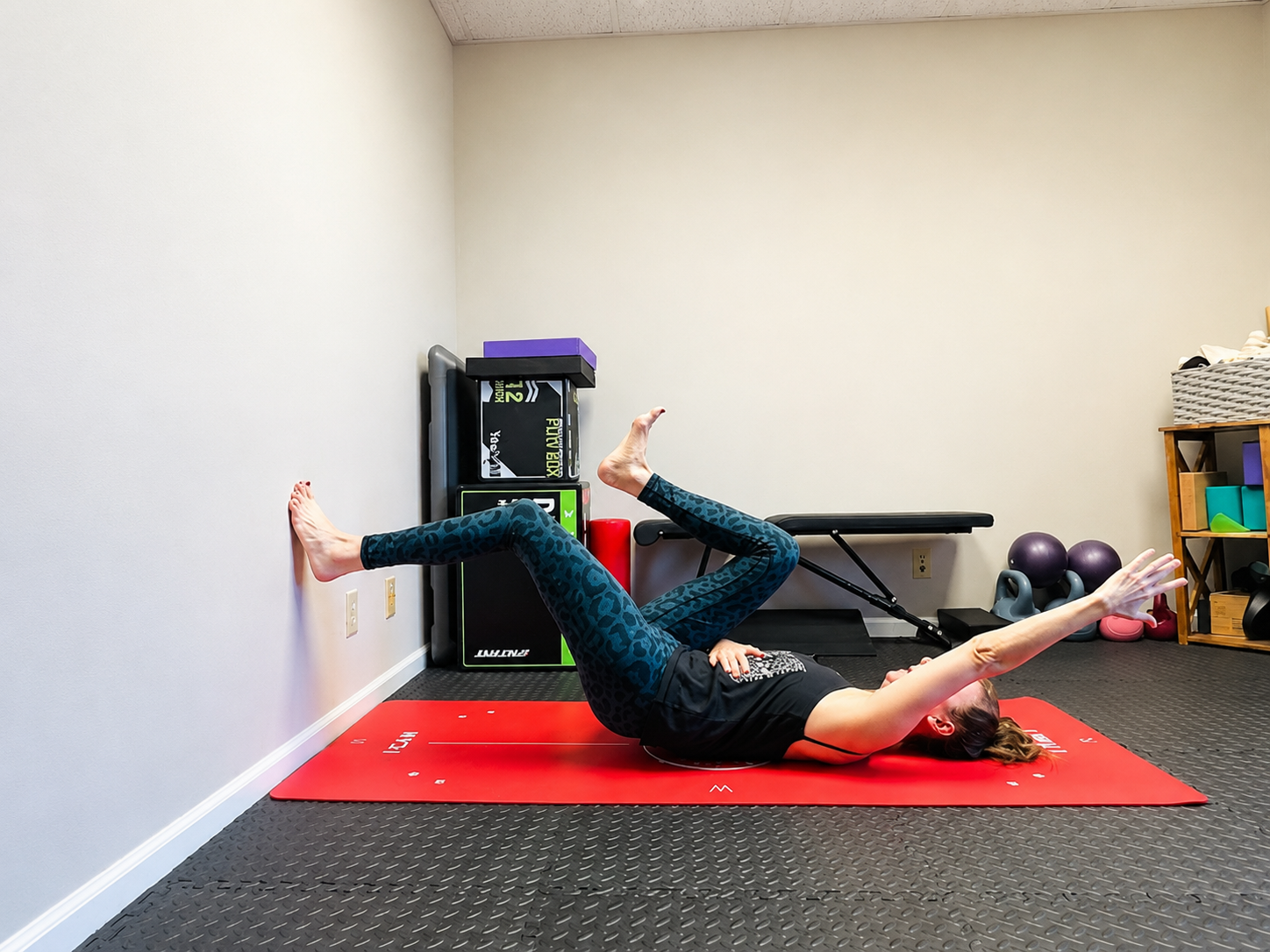 Woman practicing a wall-supported core and breathing exercise on a red mat.