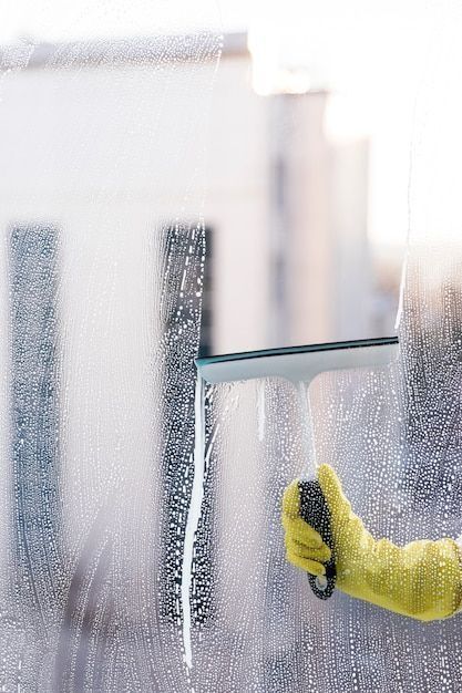 Person in yellow gloves cleaning a foggy window with a squeegee