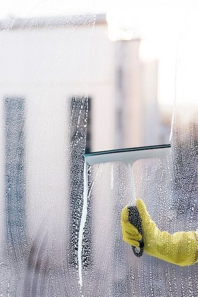 Hand in yellow glove using a squeegee to clean a wet window pane.