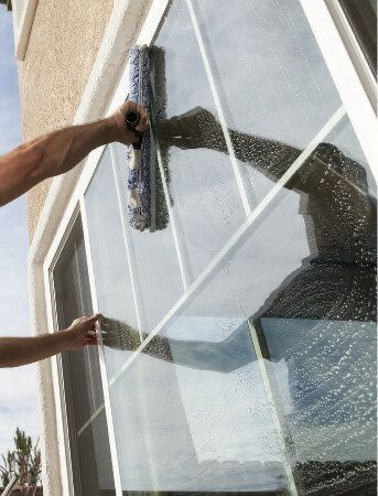 Worker cleaning a large window with a squeegee outside a building