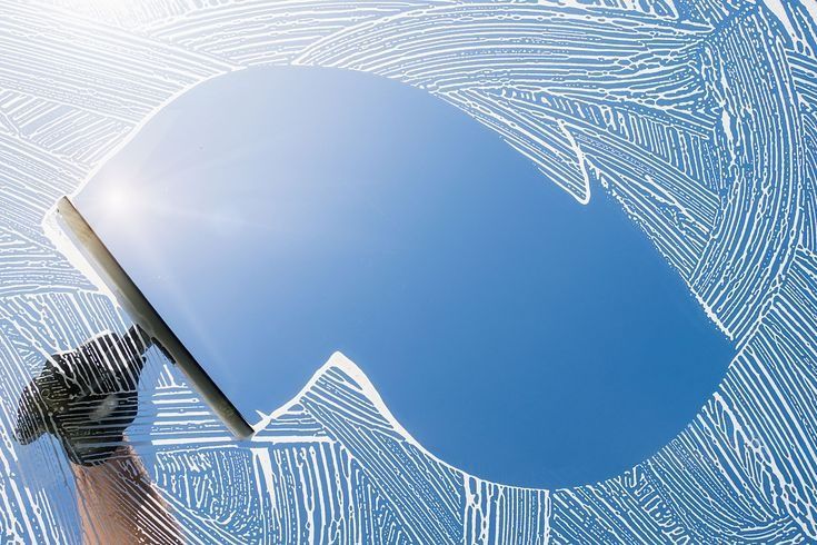 Hand holding a squeegee cleaning frosted blue glass with white streaks.
