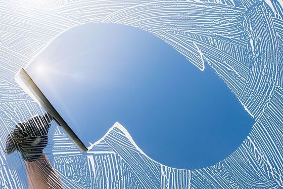 Hand wiping a blue windshield with a squeegee, leaving clean streaks across the glass