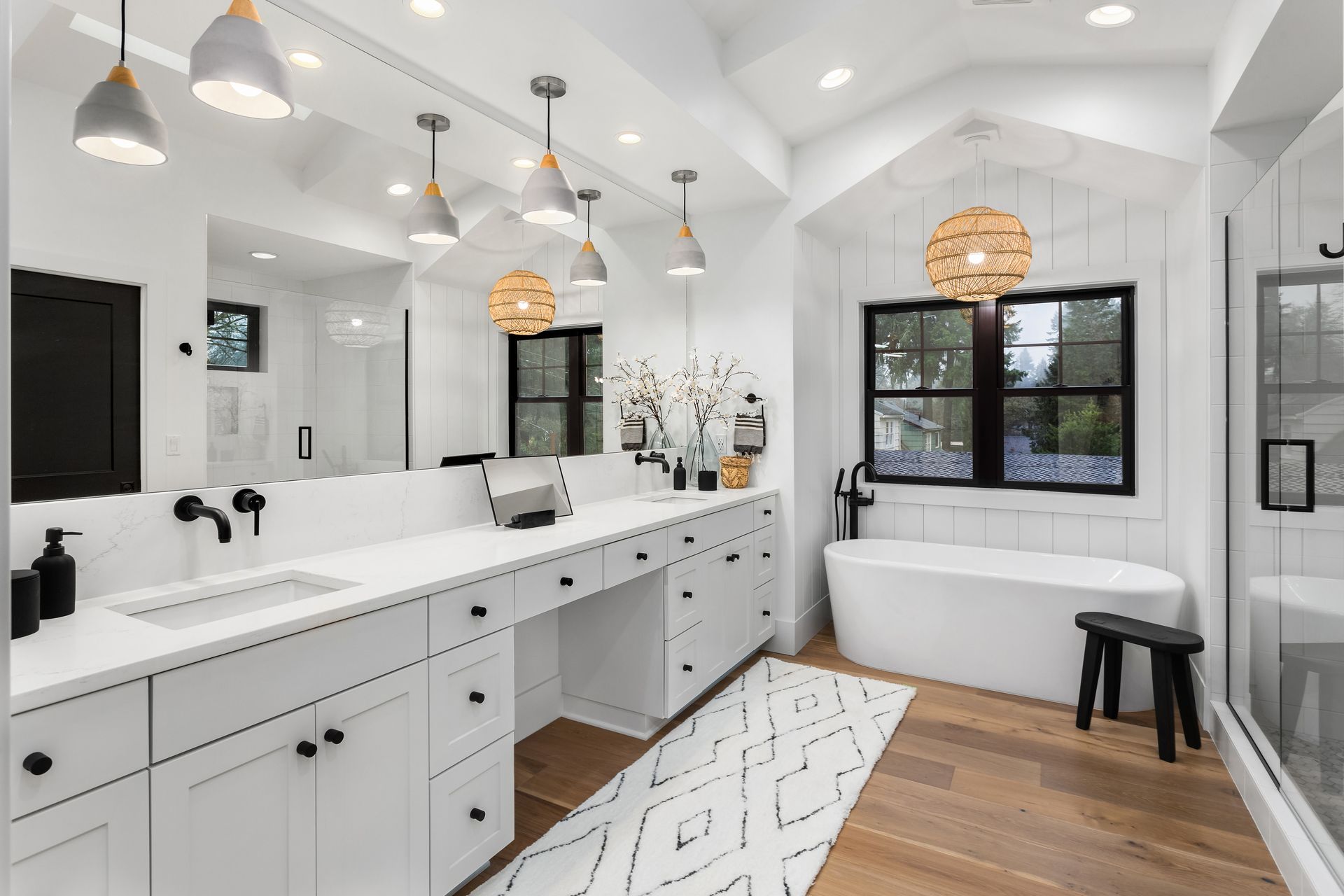 White modern bathroom with double vanity, bathtub, black accents, and pendant lighting.