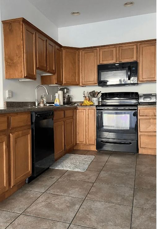 Kitchen with brown cabinets, black appliances, and tile floor.