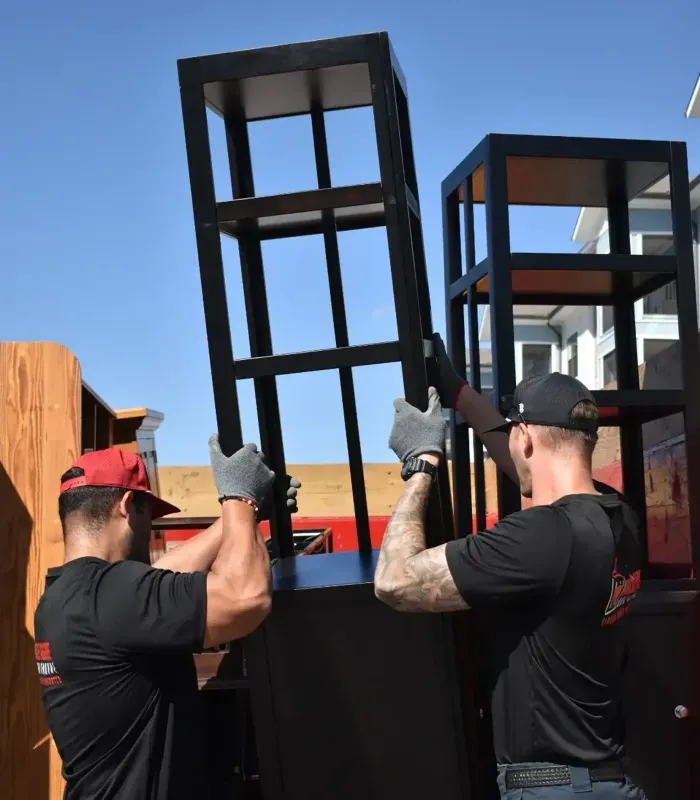 Two people in gloves lift a black frame outdoors under a clear blue sky.