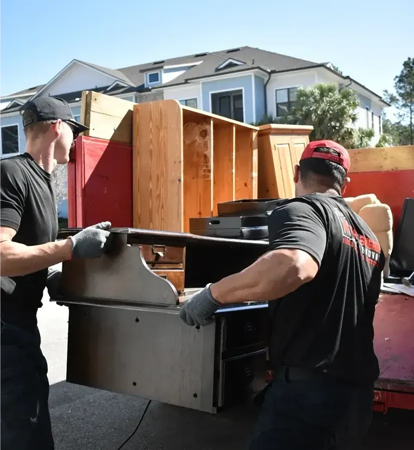 Workers moving furniture and wooden cabinets from a truck in a suburban driveway