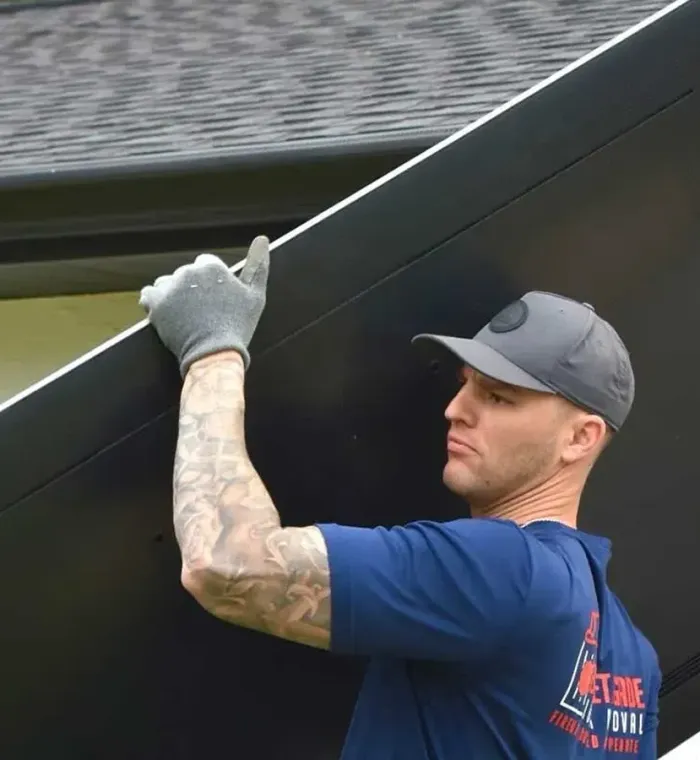 Worker in blue shirt and gray cap lifting a large black panel outdoors