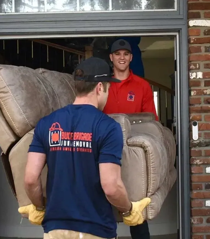 Two movers carrying a beige couch through a brick house doorway