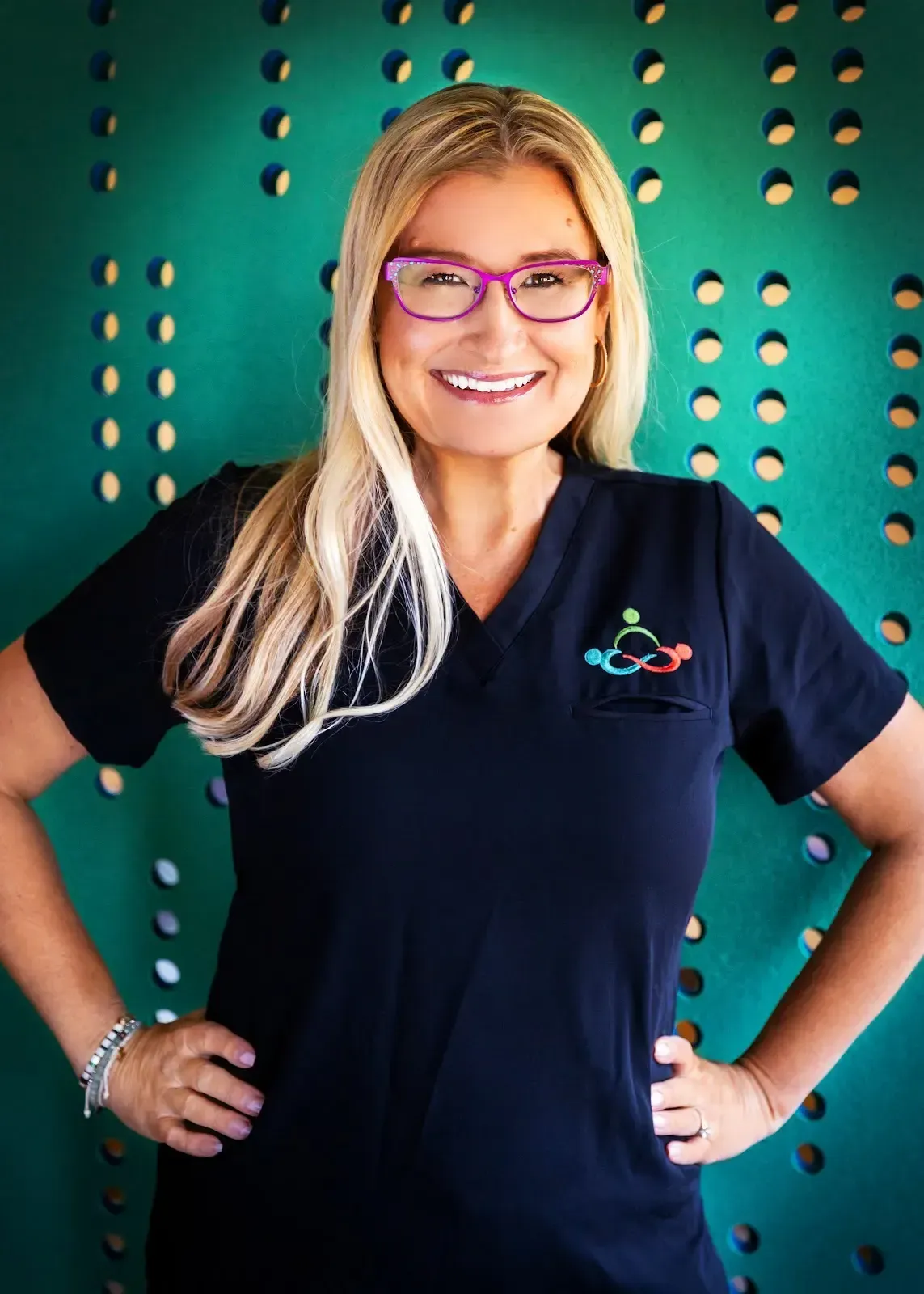 A photo of Dr. Jill Jenkins smiling at the camera. She has blond hair, brown eyes, and pink glasses.