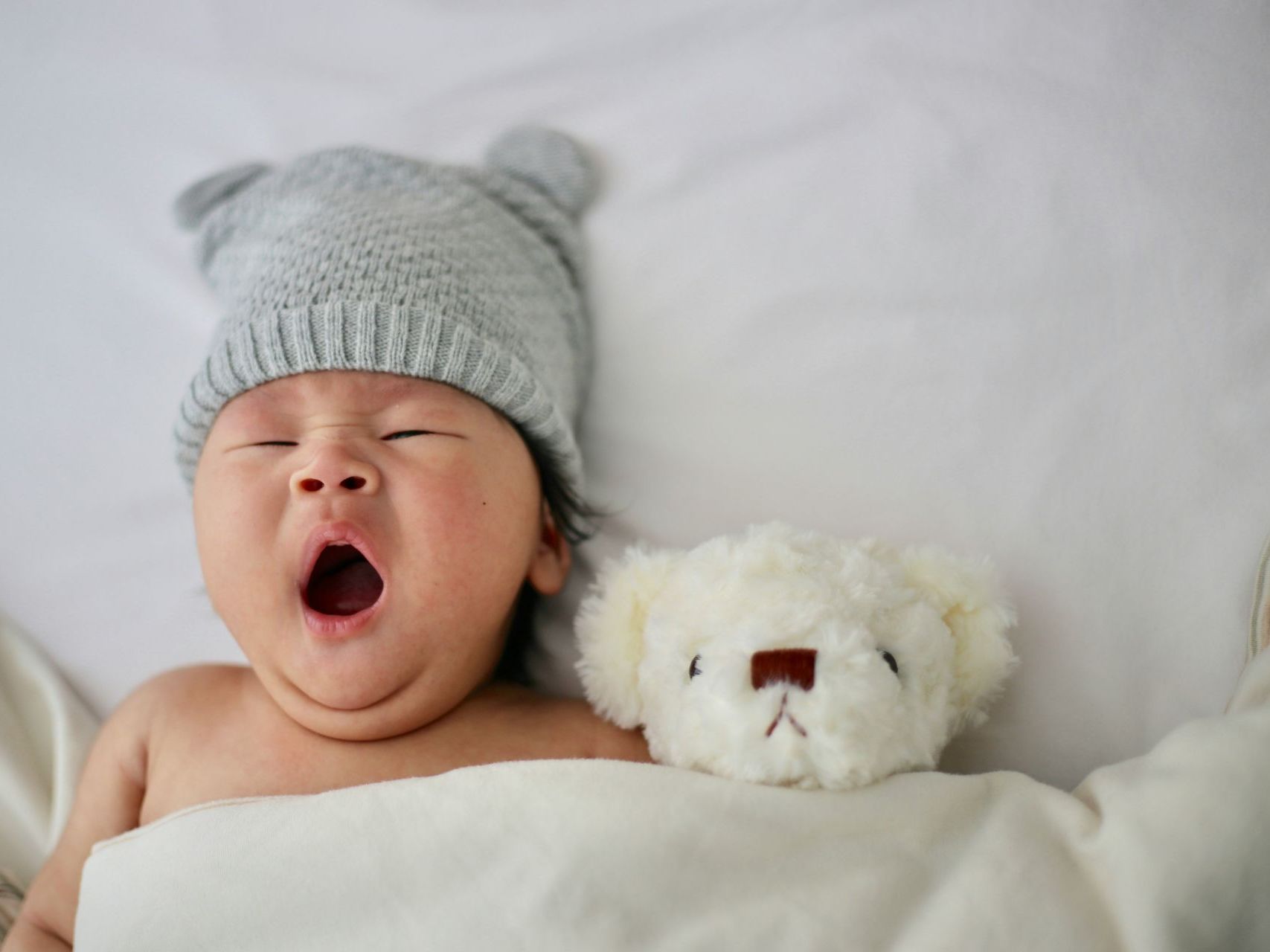 a baby wearing a hat is yawning next to a teddy bear .