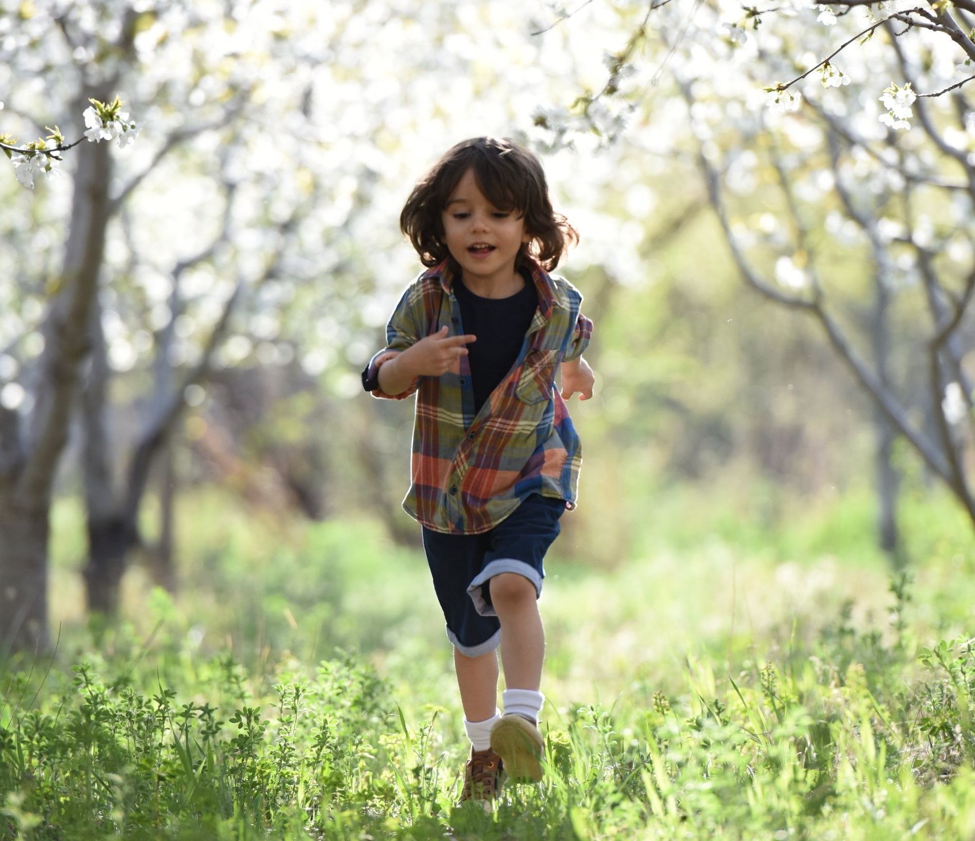 a young boy is running through a field with trees in the background .