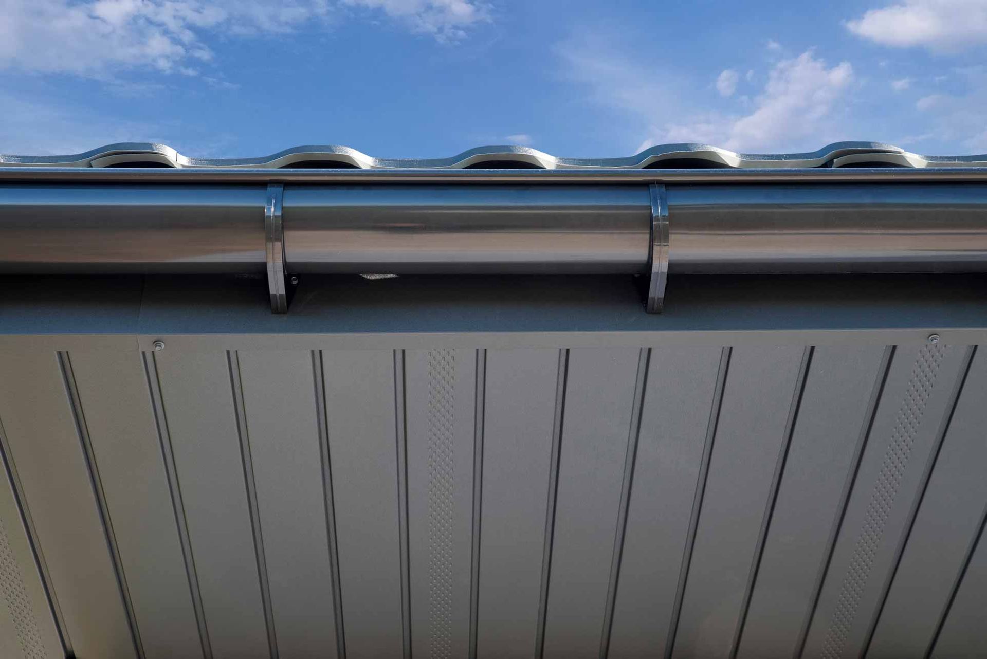 Close-up of a roof edge with silver guttering against a blue sky