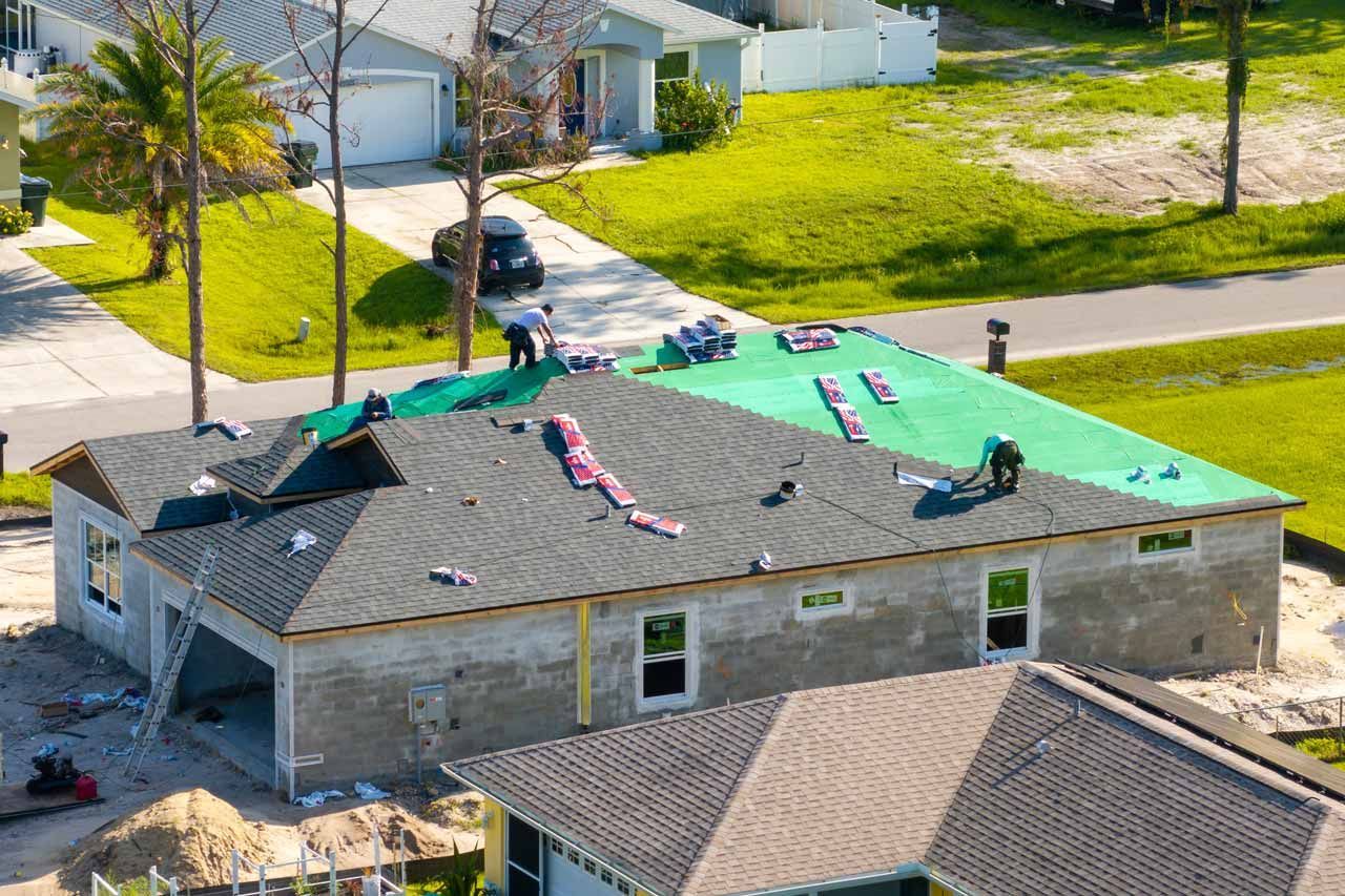 Workers fixing a house roof with green tarps and pink insulation in a suburban neighborhood