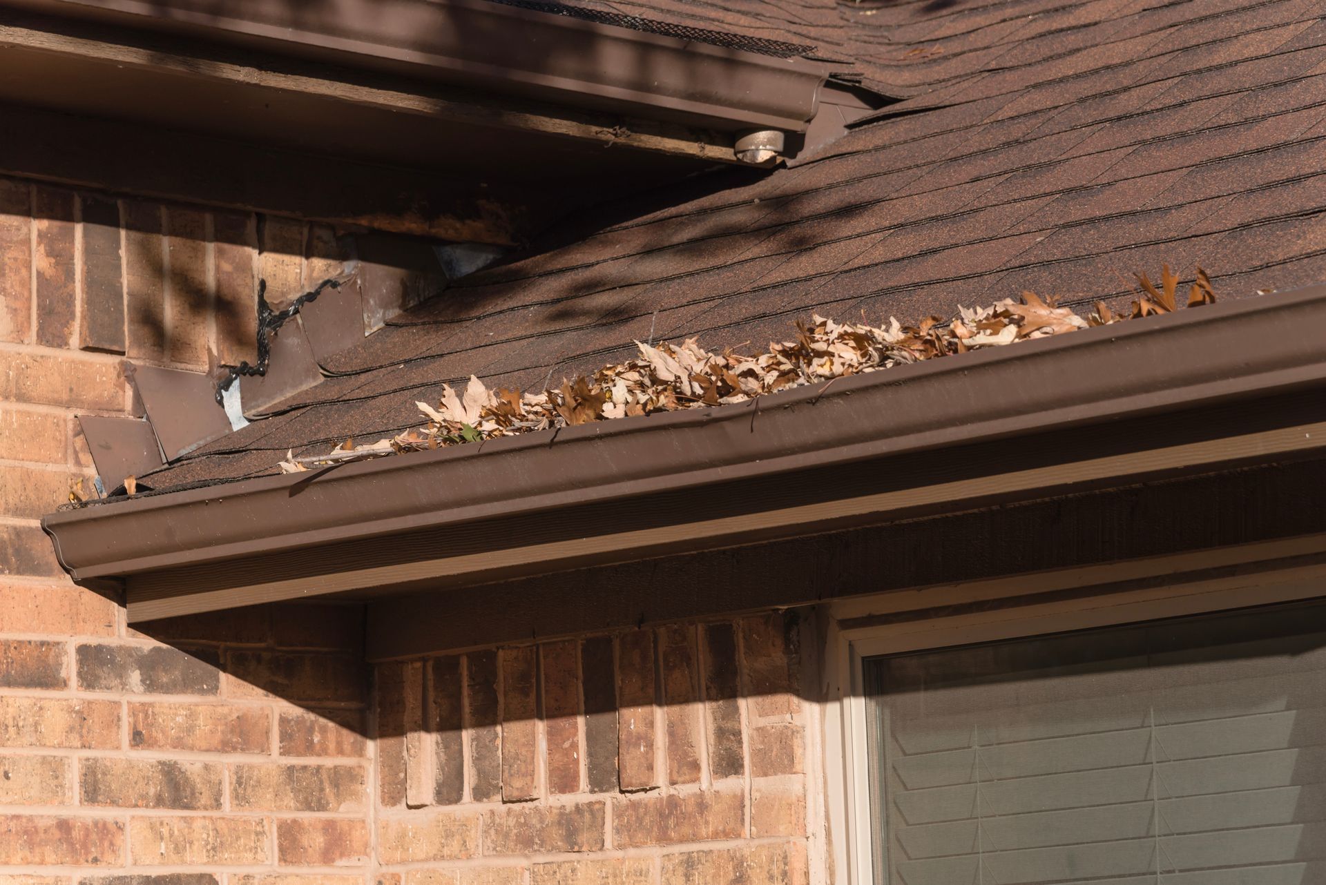 Damaged brick house roof edge with exposed underlayment and debris along the gutter