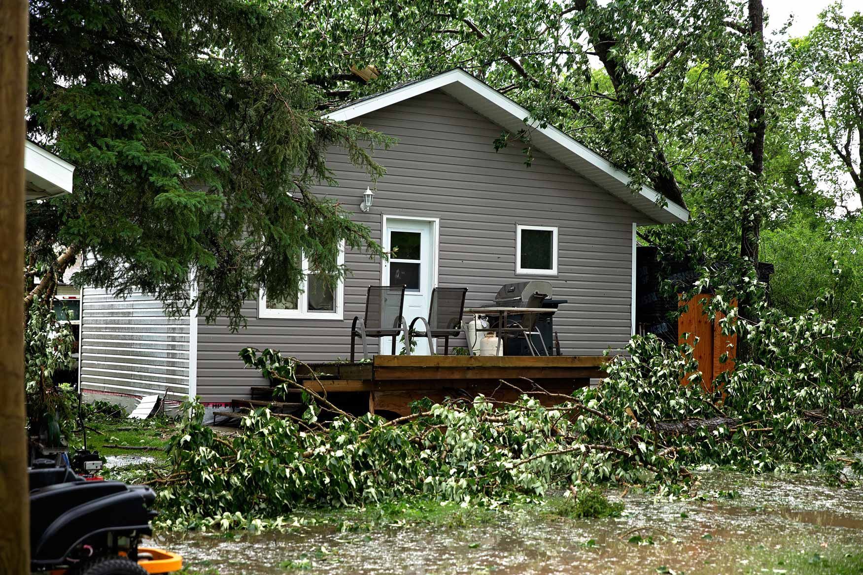 Gray house with a wooden deck and fallen branches in a wooded yard after a storm
