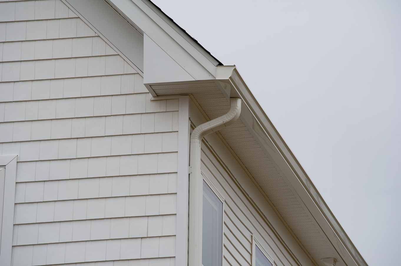 White house roof corner with gutter and downspout against a gray sky