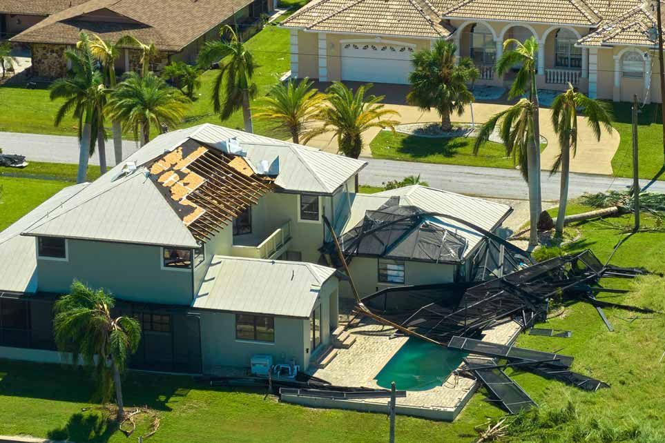 Collapsed backyard screen enclosure beside a house after storm damage, with broken roof panels and debris.