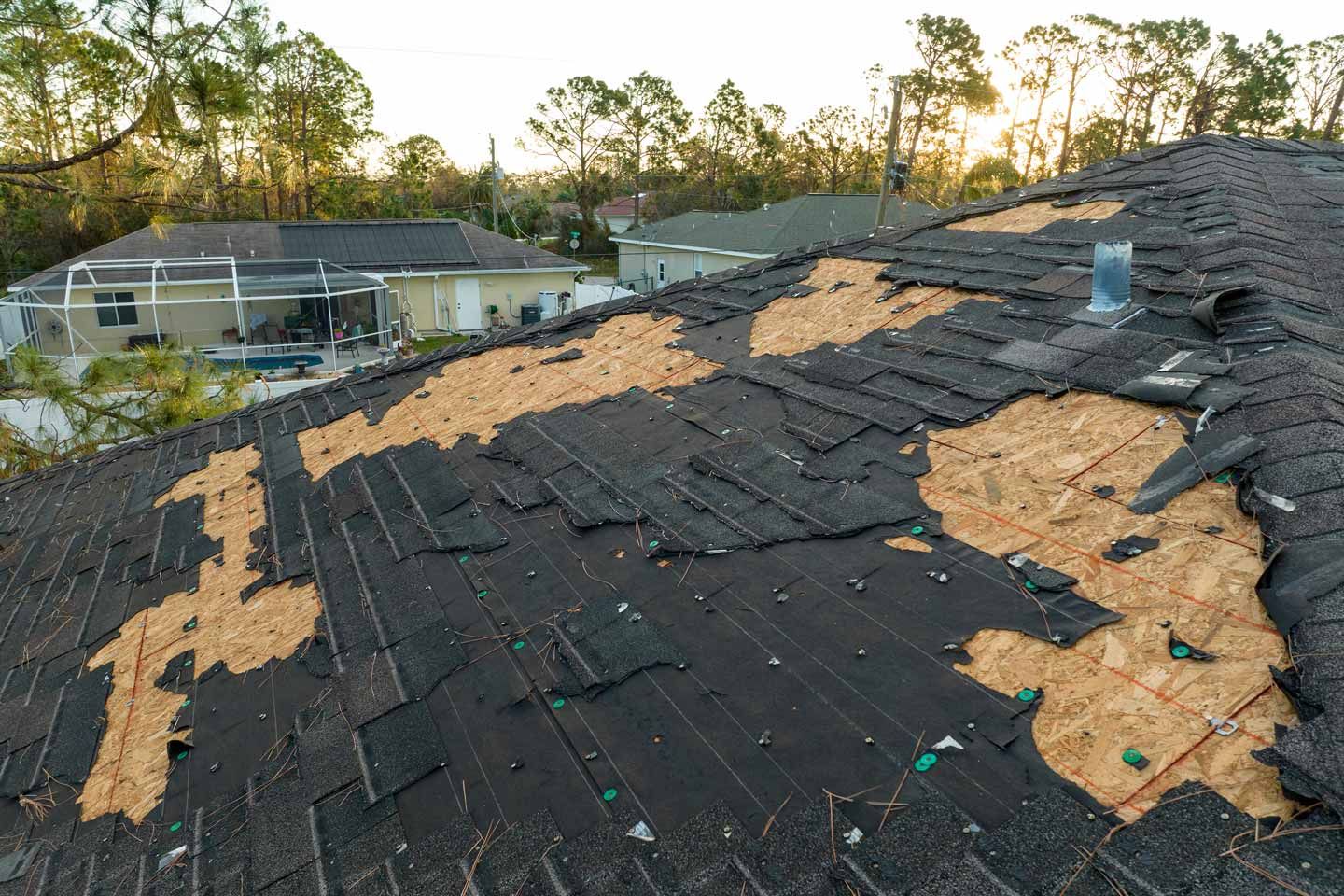 Damaged rooftop with missing shingles and exposed wood under evening light
