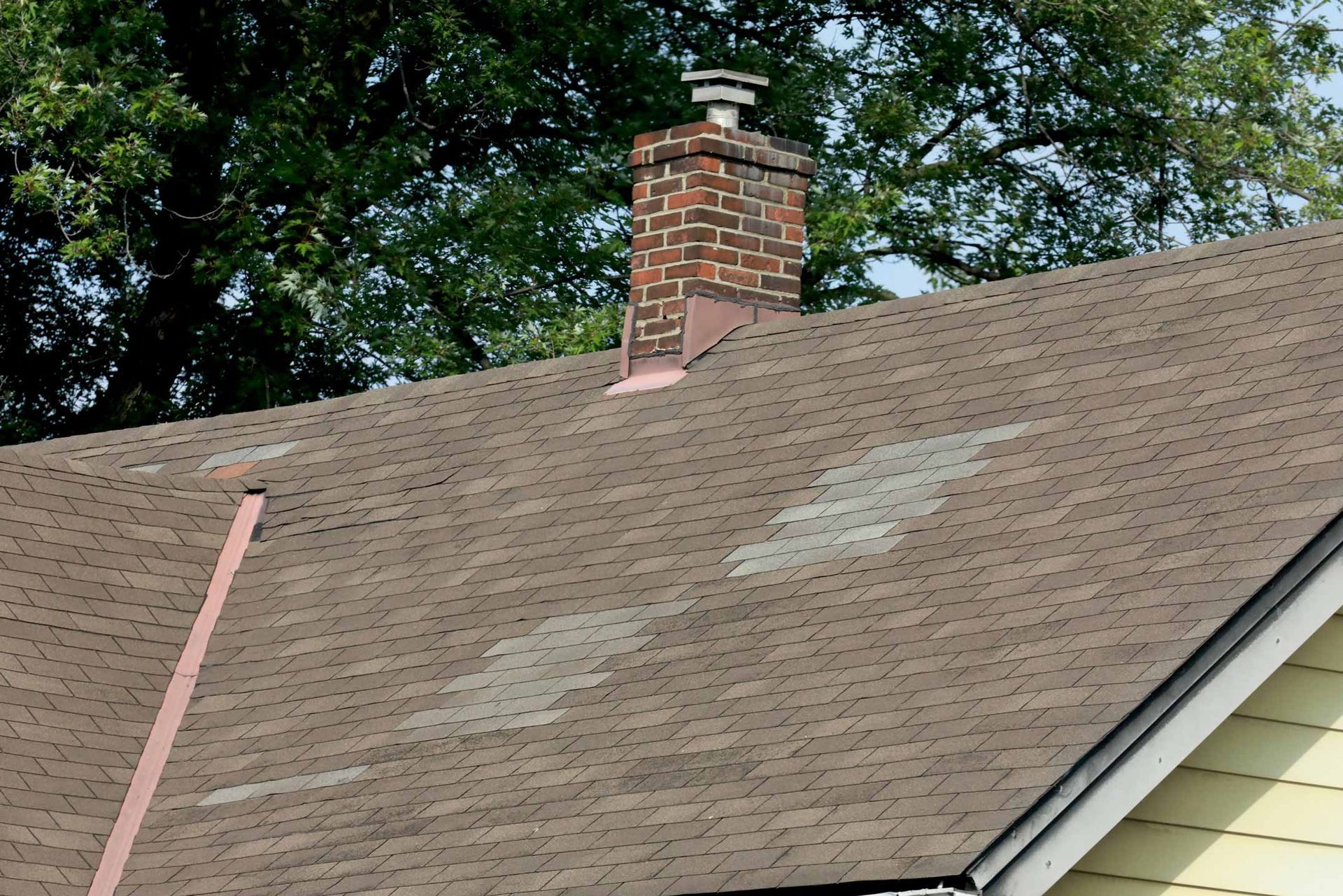 Roof with chimney and patchy shingles beneath trees