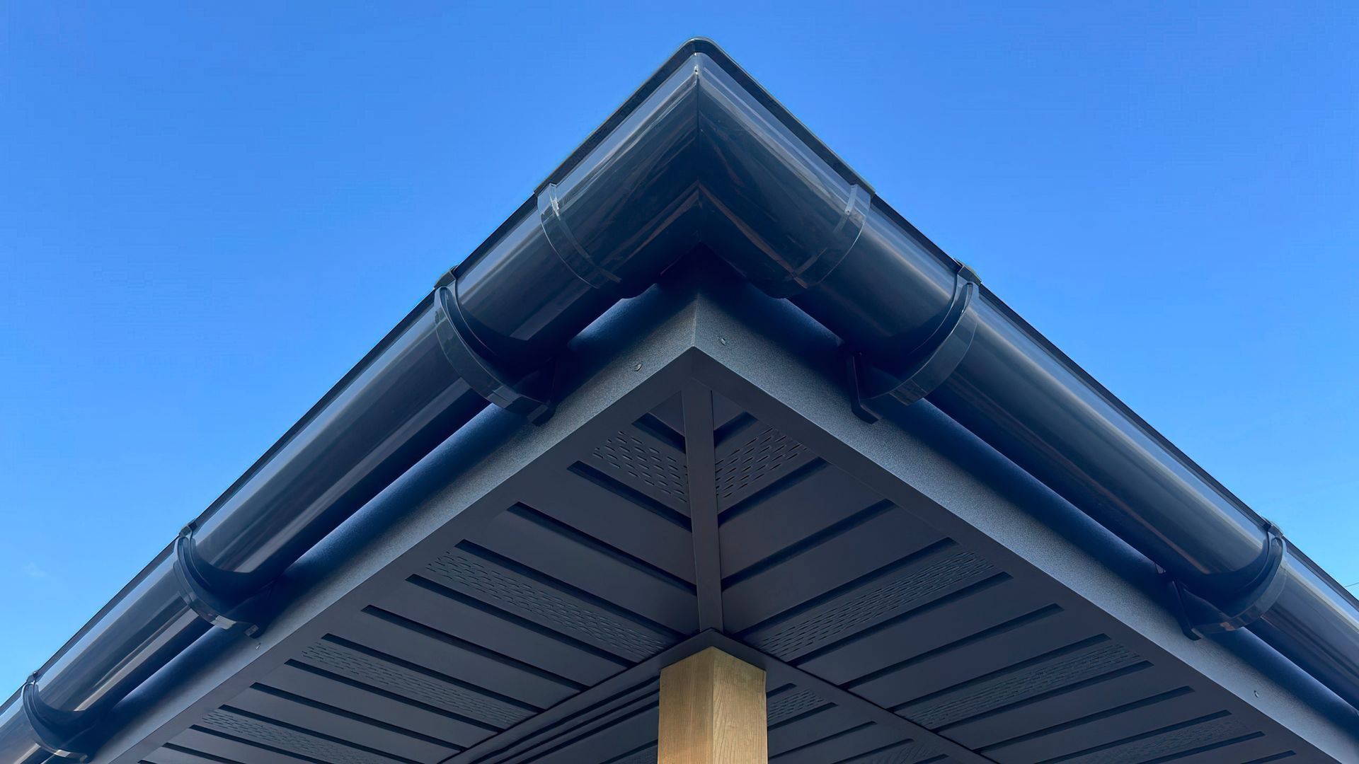 Close-up of a house roof peak with dark gutters against a clear blue sky