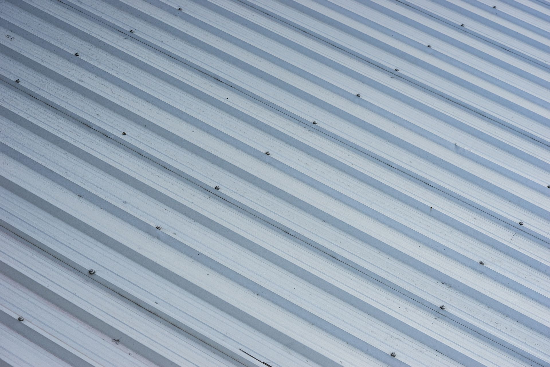 Close-up of a light gray corrugated metal roof with diagonal ridges and small fasteners