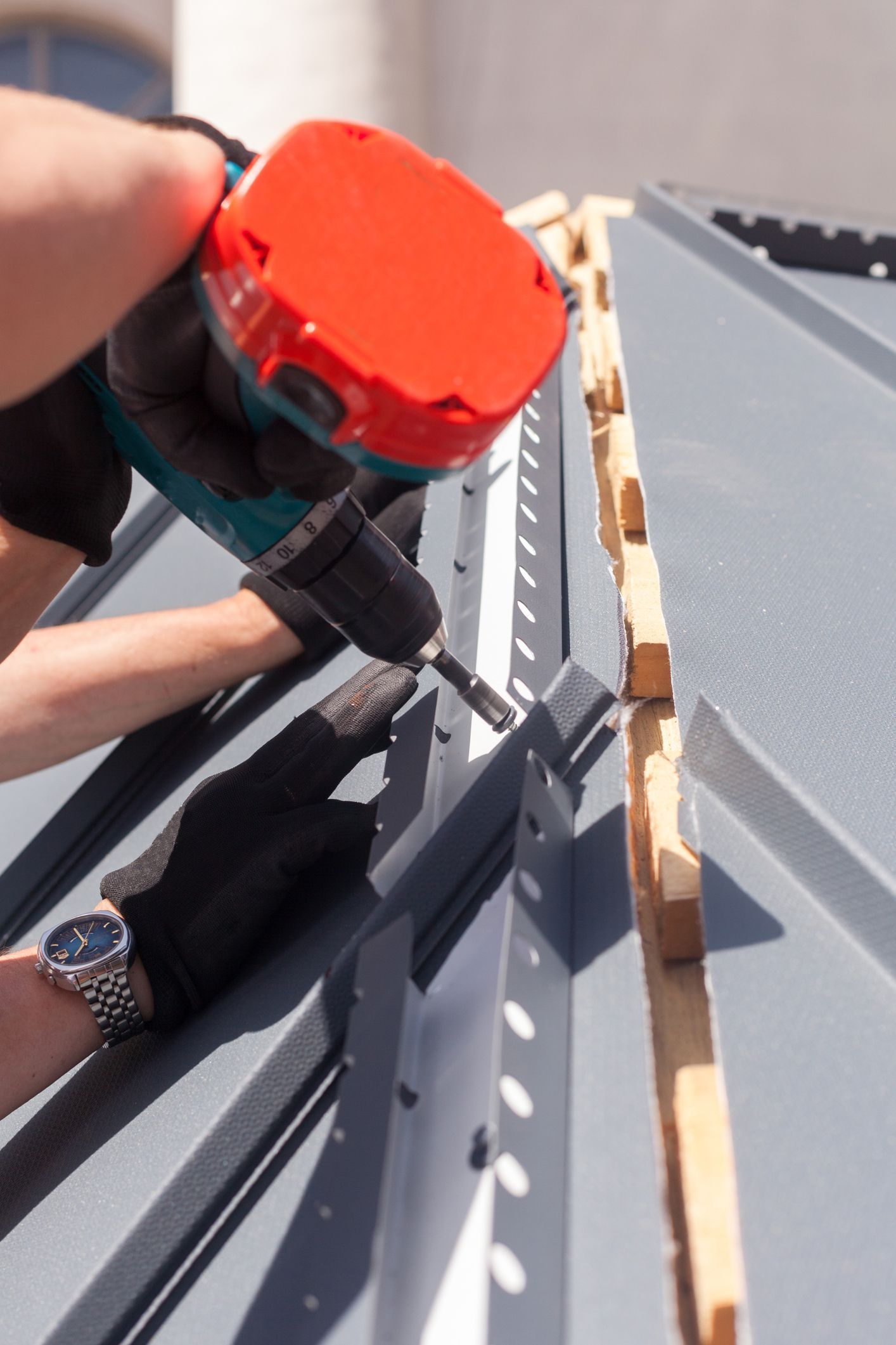 Person painting a rooftop seam with a red paint applicator and black tool hose