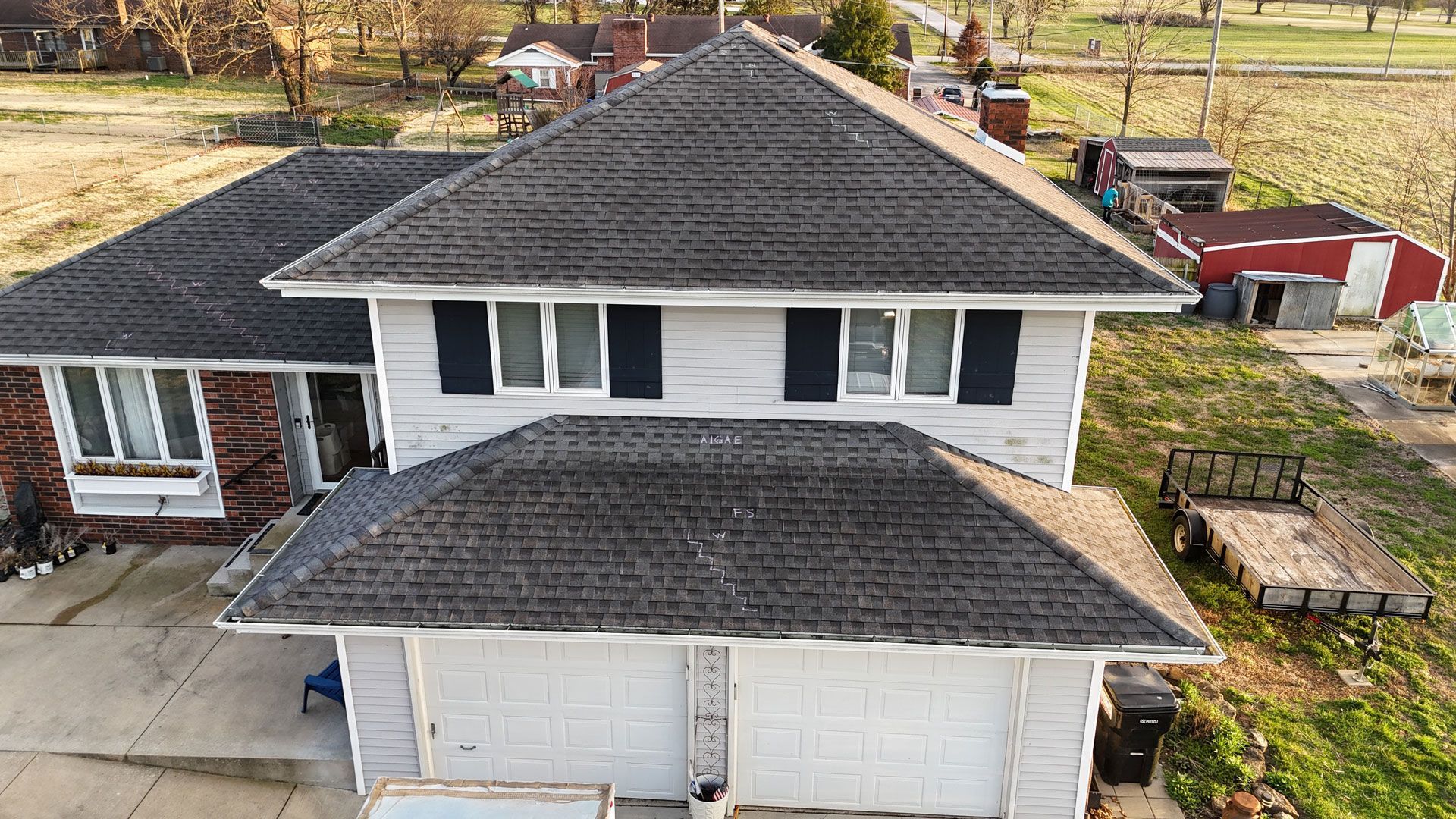 Aerial view of a white two-story house with dark shingled roofs and a double garage, surrounded by a yard.