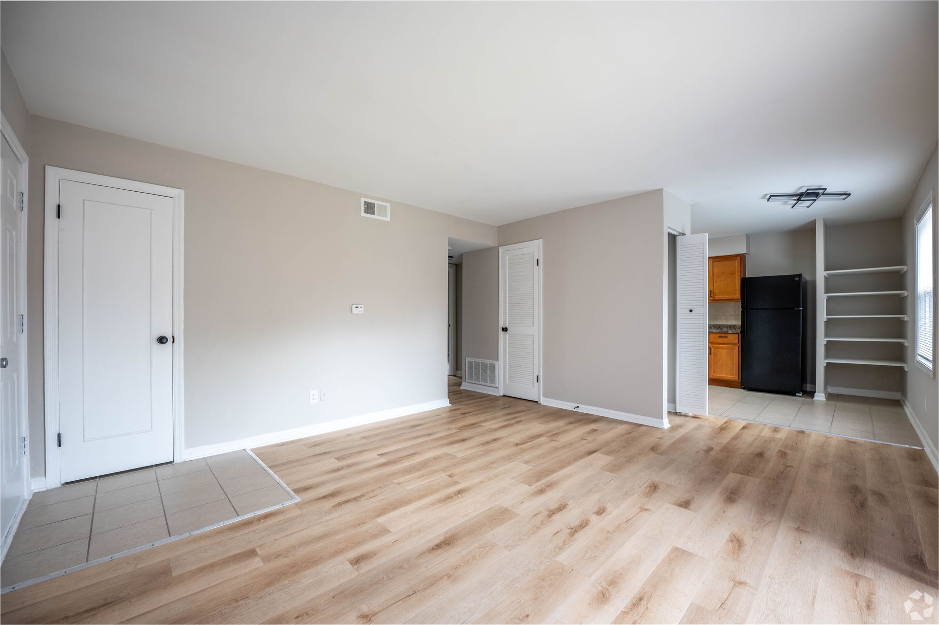Empty living room with light wood floors, beige walls, and white doors.
