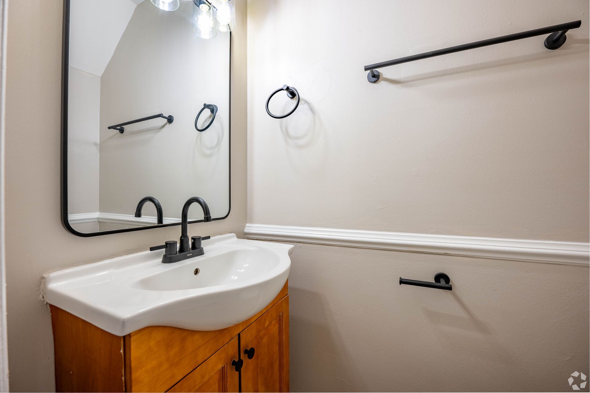 Bathroom with a white sink, black faucet and fixtures, wooden cabinet, and a mirror.