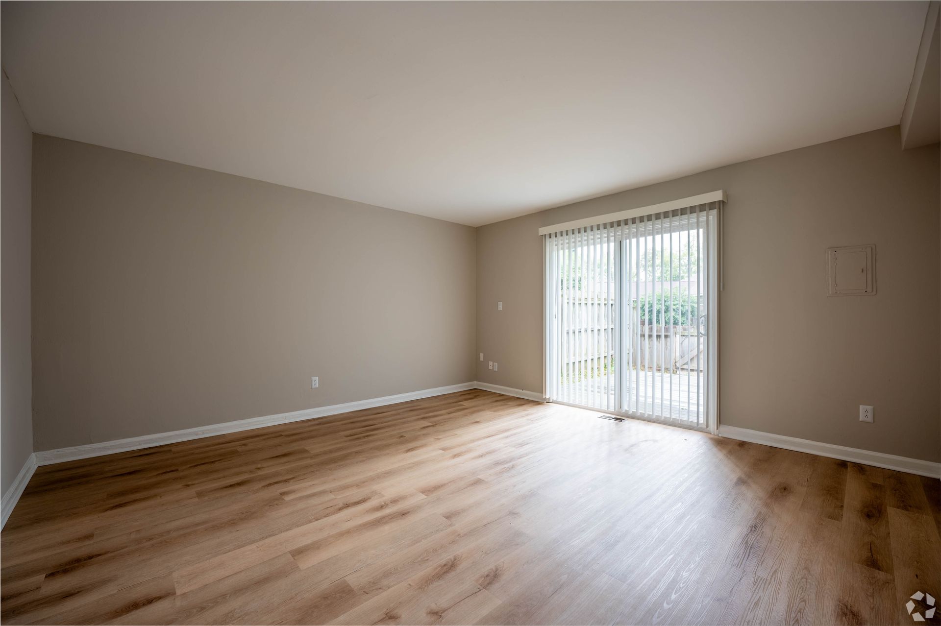 Empty room with wood floors, beige walls, and a sliding glass door.