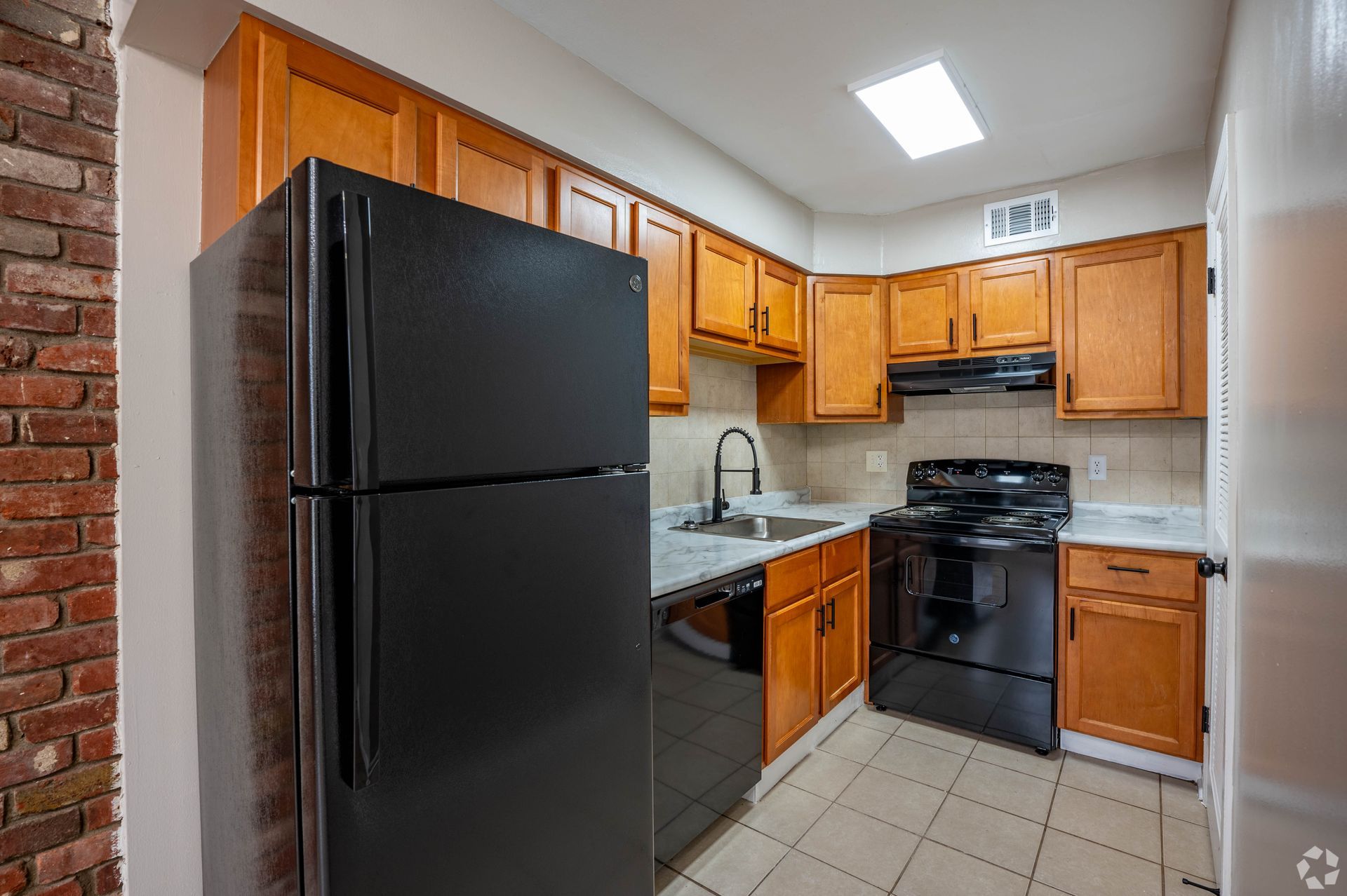 Kitchen with wood cabinets, black appliances, and brick accent wall.