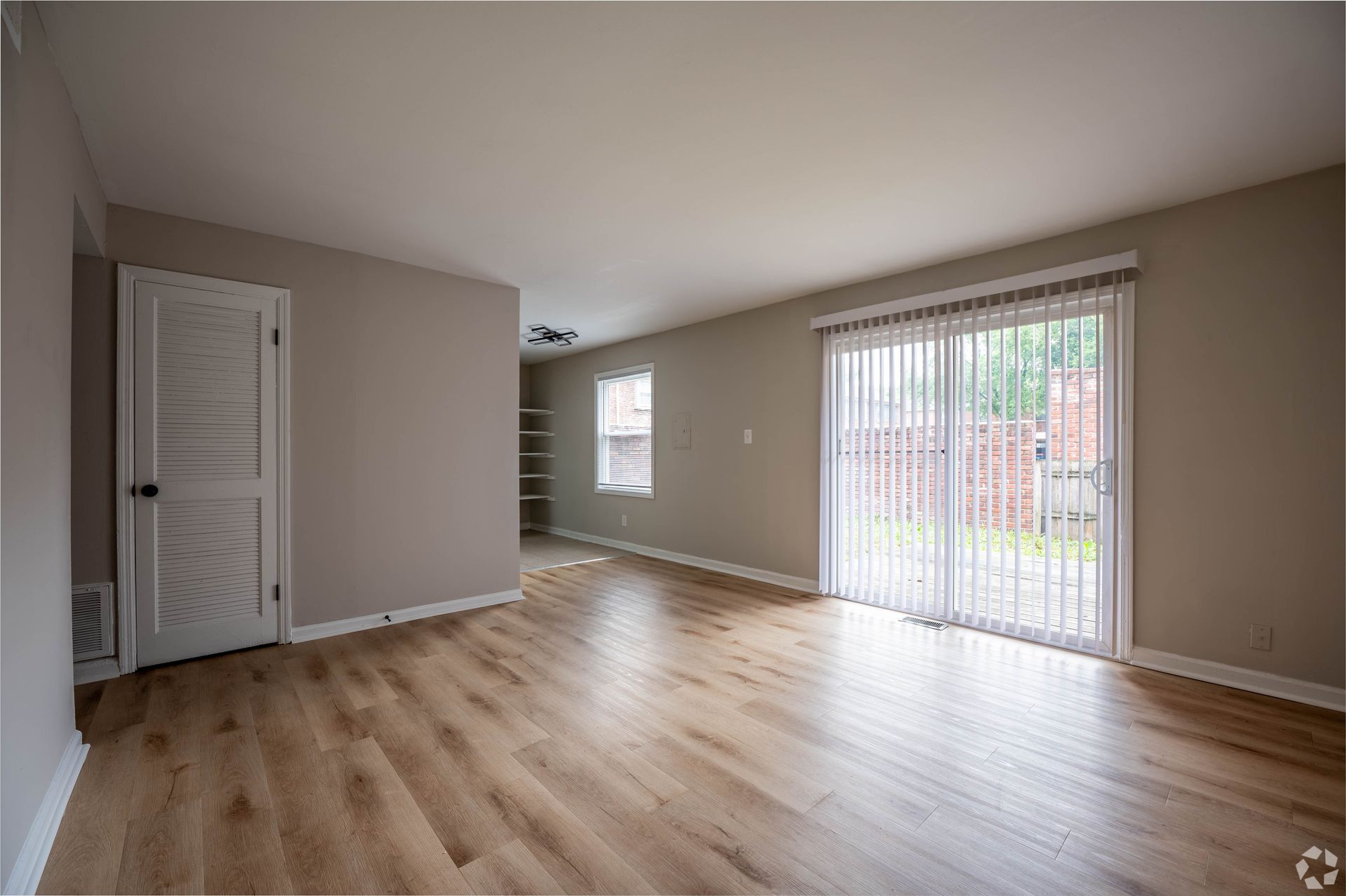 Empty living room with wood-look floor, sliding glass door, and a closed door, with neutral color walls.