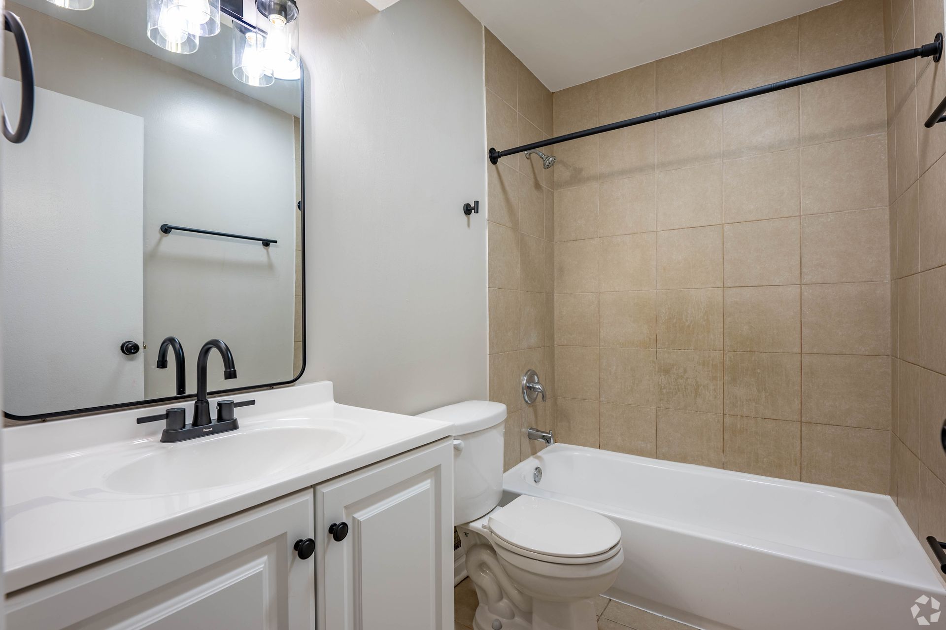 Bathroom with white vanity, toilet, and bathtub. Beige tile and black fixtures.