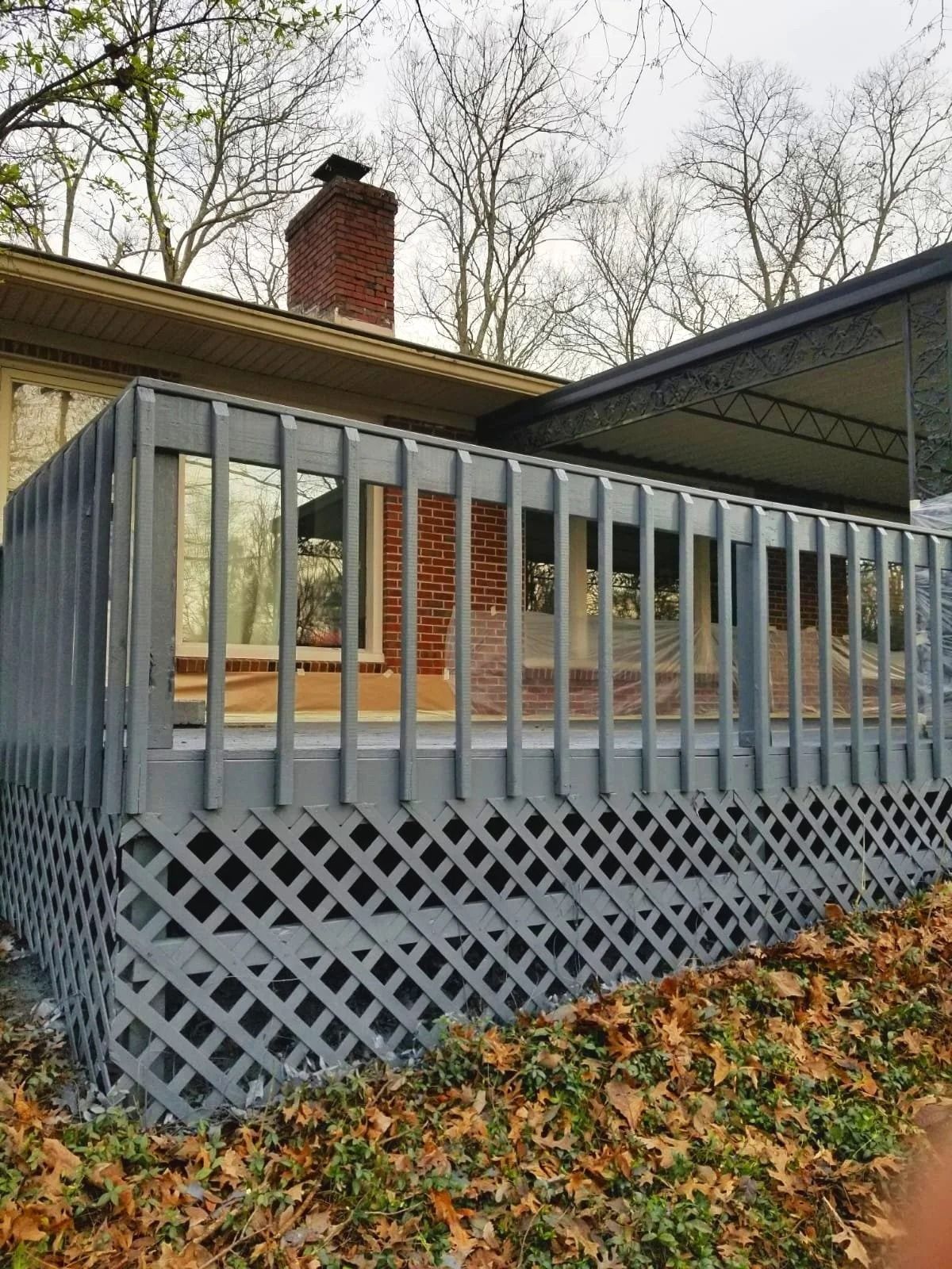 Gray painted deck with lattice skirting, against a house and under trees.