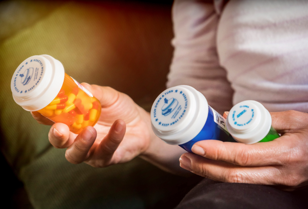 Hands holding three prescription pill bottles, including one orange bottle and two white-and-blue bottles.