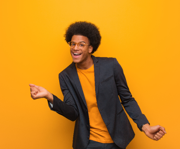 Smiling person in a dark blazer and an orange shirt dancing against a bright orange background