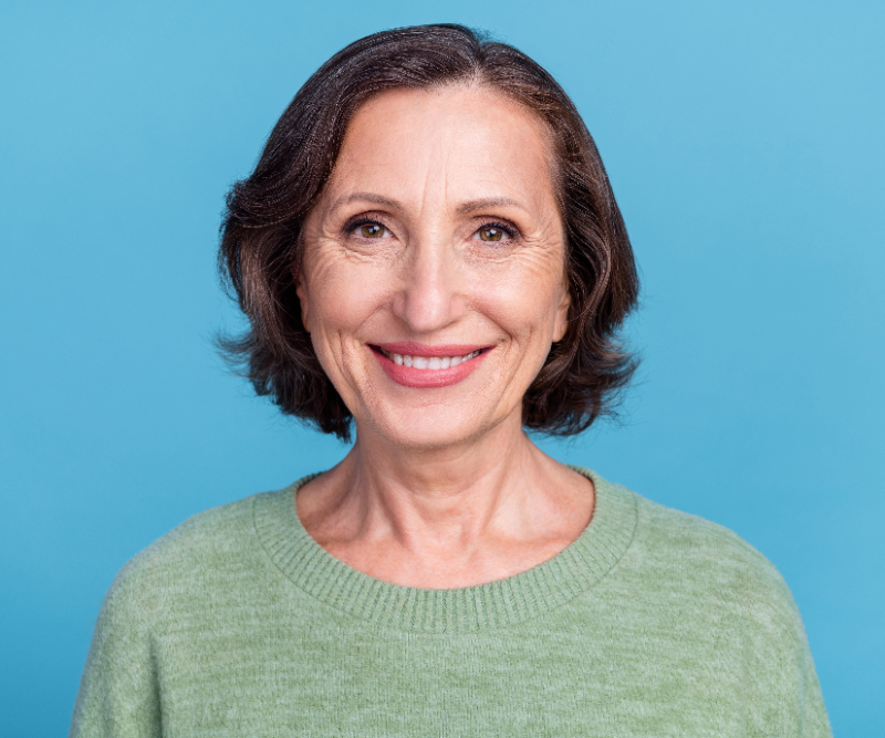 Smiling woman with short dark hair wearing a light green sweater against a blue background