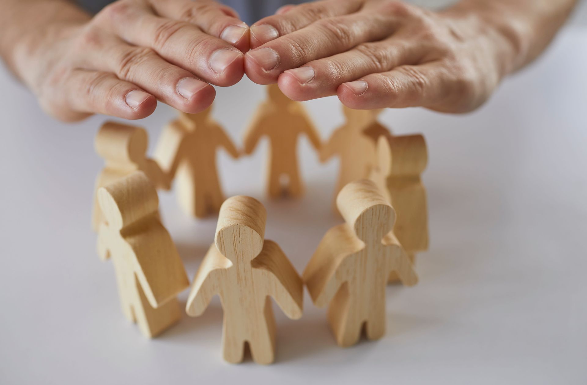 Hands sheltering wooden figurines in a circle, symbolizing protection and community