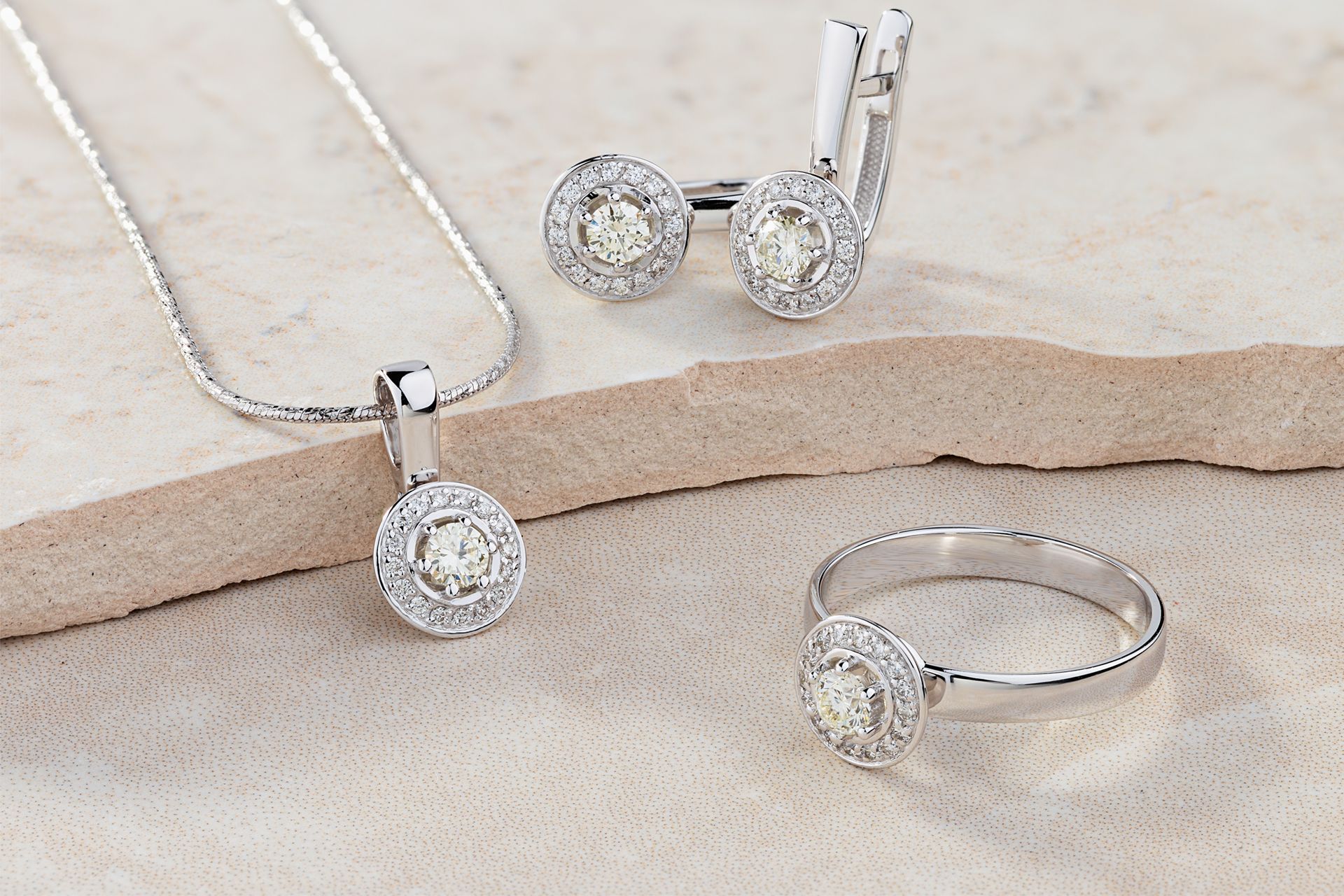 Silver diamond jewelry set with necklace, earrings, and ring on a beige surface