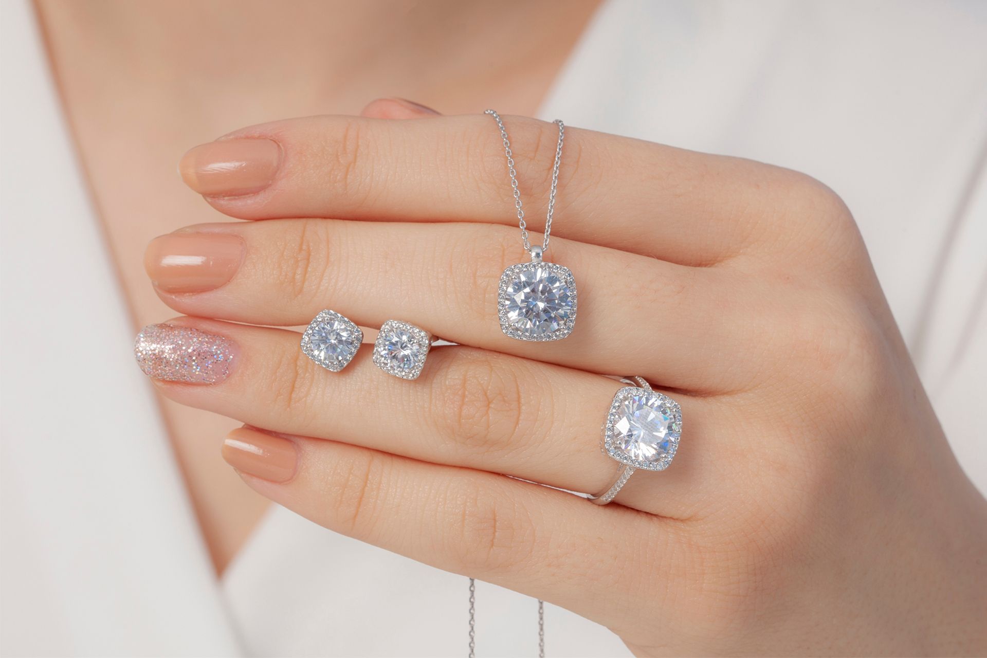 Hand wearing silver diamond rings and a matching pendant necklace against a soft pink background