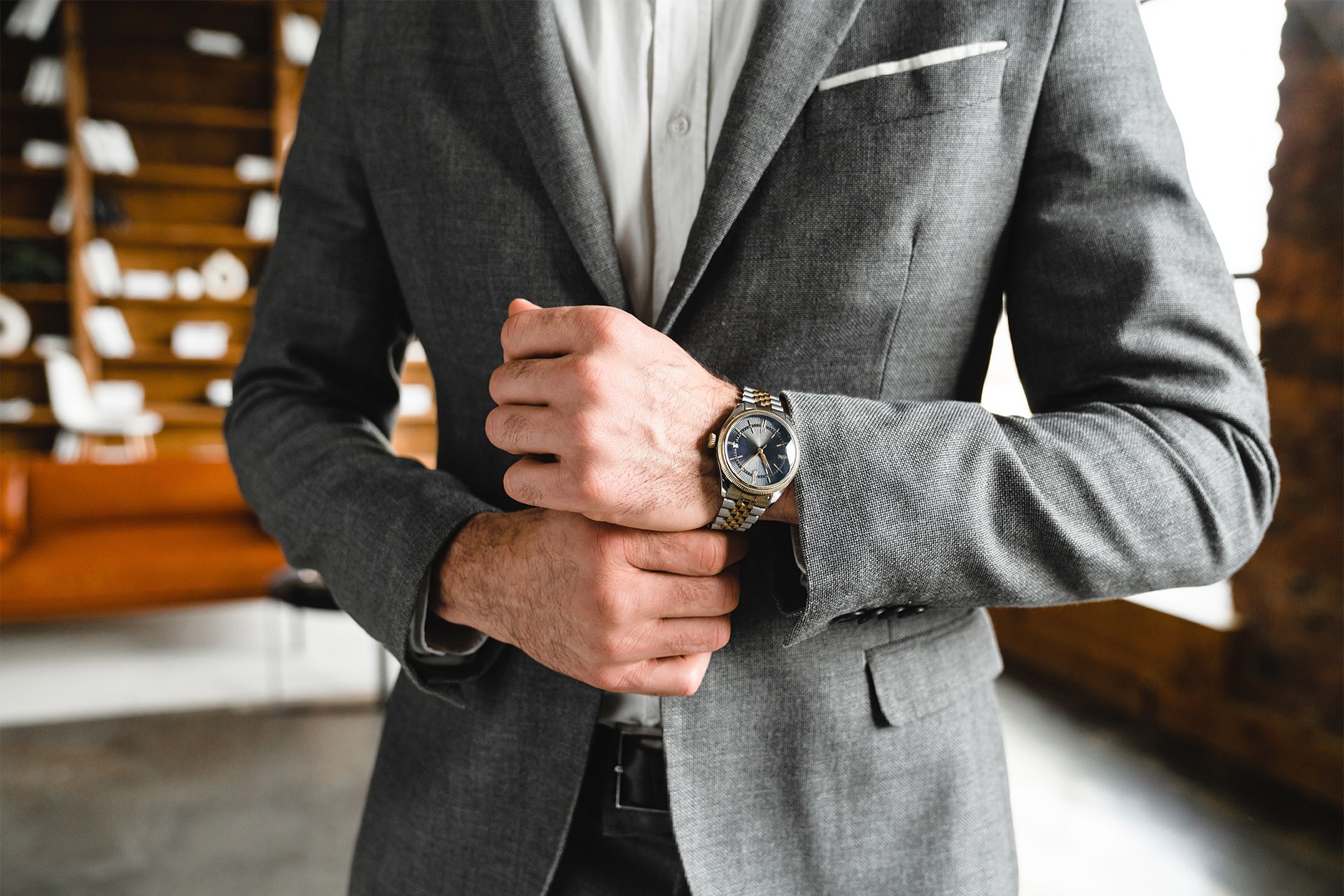 Man in gray suit adjusting his jacket in a warm, blurred indoor setting