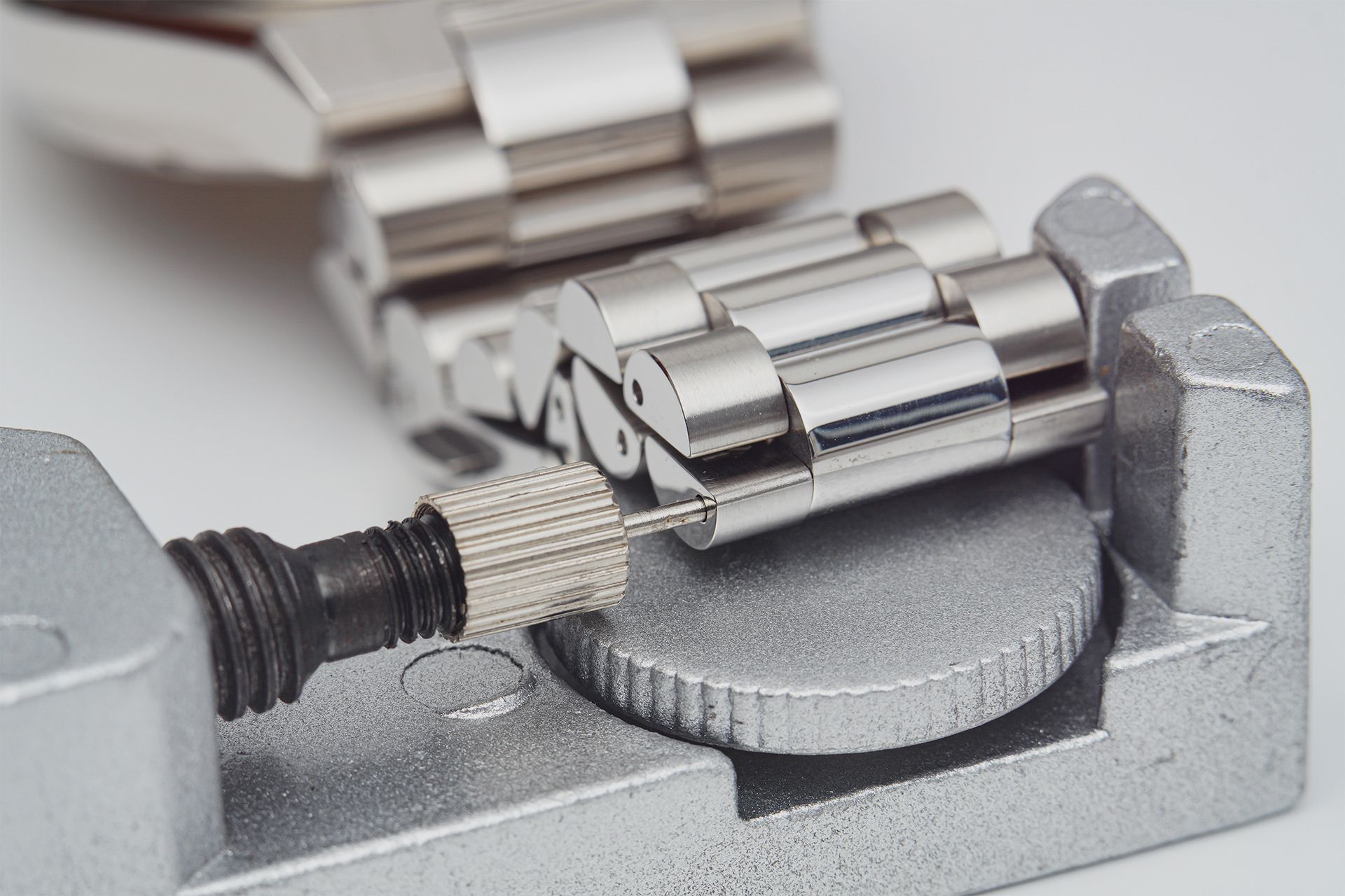 Close-up of a metal watch band repair tool adjusting a silver watch link