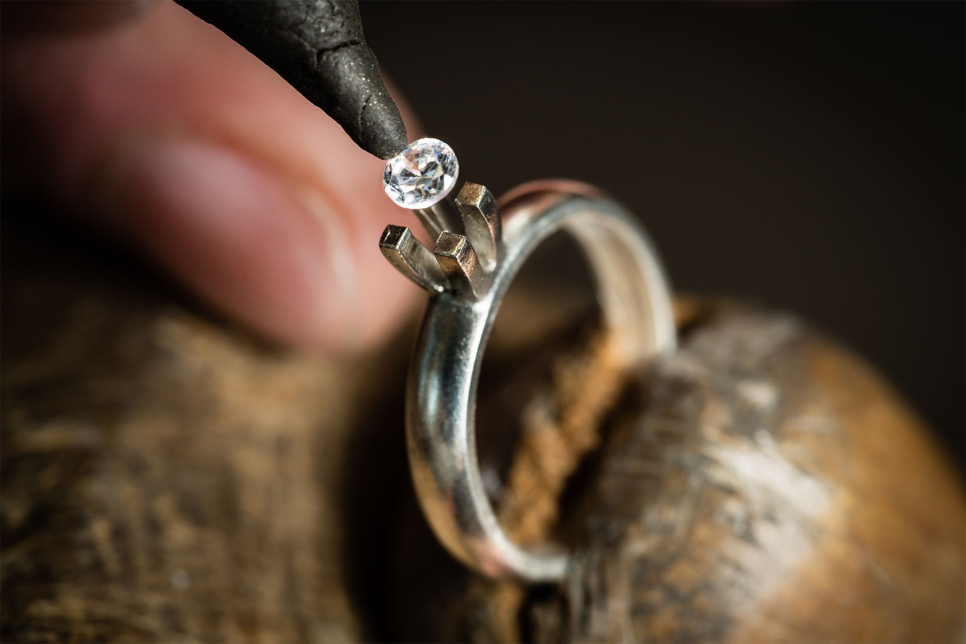 Diamond engagement ring held by fingers over a wooden surface