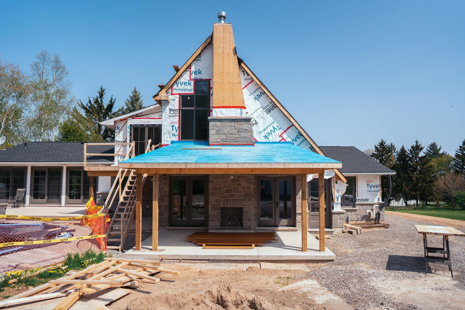 House under construction; stone fireplace, wood beams, blue roofing, unfinished exterior.